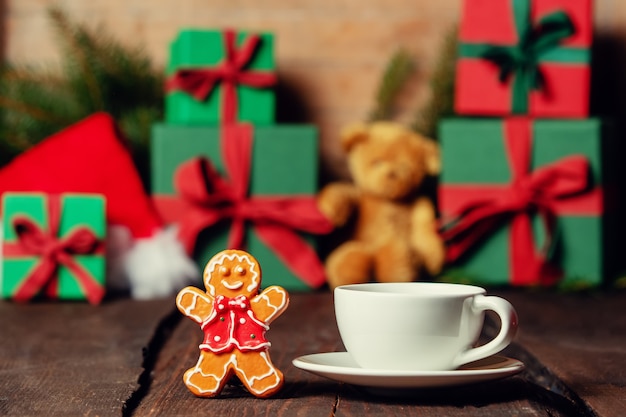 Tasse Kaffee und Lebkuchenspielzeug auf Holztisch mit Geschenken im Hintergrund