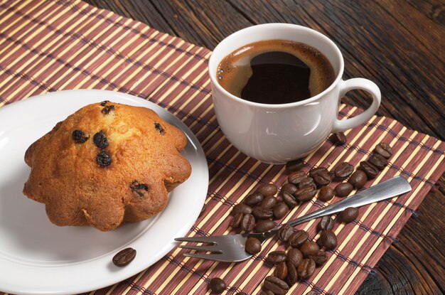 Tasse Kaffee und Muffin mit Rosinen in der Platte auf Hintergrund der Bambusserviette