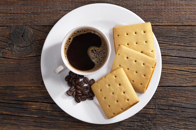 Tasse Kaffee und quadratische Kekse mit Marmelade im Teller zum Frühstück auf der Holztischplatte