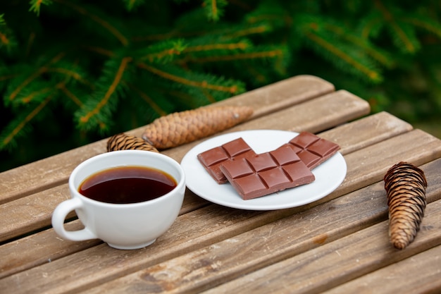 Tasse Kaffee und Schokoriegel auf Holztisch mit Fichtenzweigen auf Hintergrund