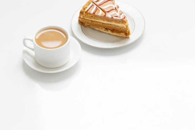 Tasse Kaffee und Stück Kuchen auf weißem Tisch