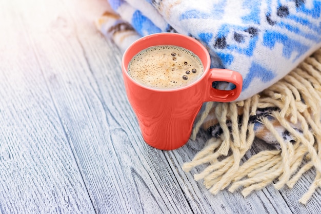 Tasse Kaffee und warme Decke mit blauem Muster auf Holztisch.