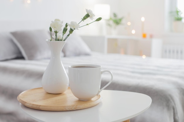 Tasse Kaffee und weiße Blumen in der Vase auf dem Tisch im Schlafzimmer