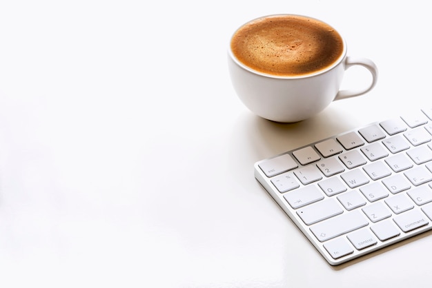 Tasse Kaffee und weiße Tastatur auf weißer Tabelle