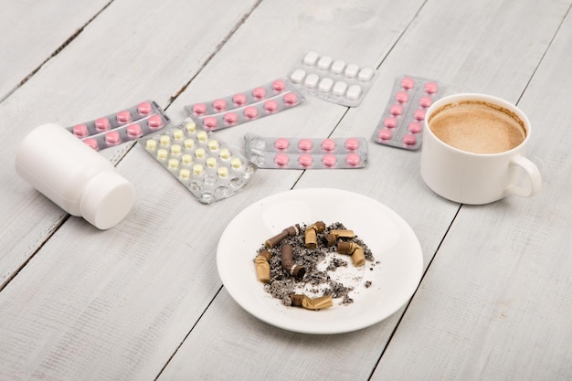 Tasse Kaffee Zigaretten medizinische Flaschen und Pillen auf weißem Holztisch