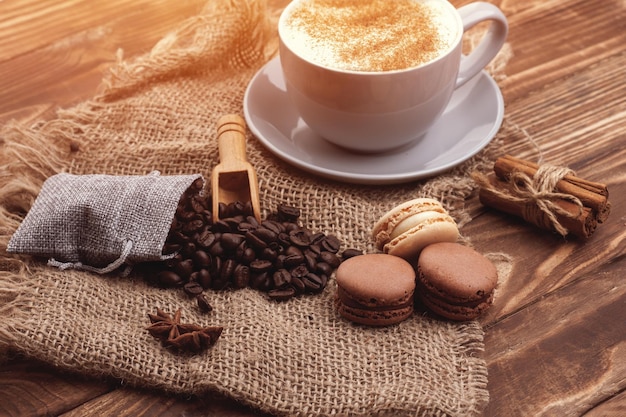 Tasse Kaffeebohnen Zimt Makronen und Anis auf dem hölzernen Hintergrund Kaffee ist die gute Idee