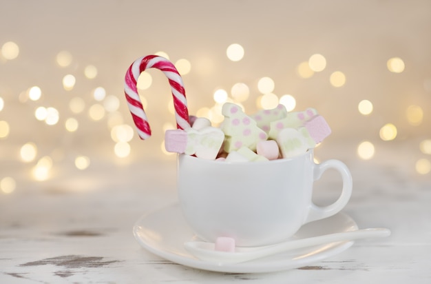 Tasse Kakao mit Marshmallows auf einem weißen Holztisch mit verschwommenen Girlandenlichtern