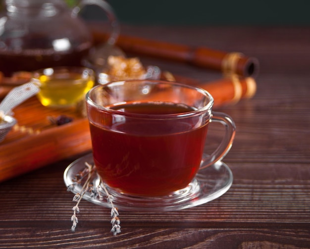 Tasse Kräutertee mit Blütenhonig in Glasteekanne und verschiedenen getrockneten Kräutern auf dem Tablett