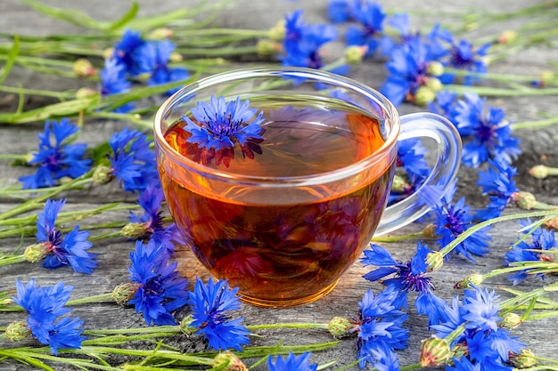 Tasse Kräutertee und blaue Kornblumenblumen auf Holzoberfläche