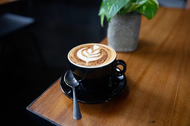 Tasse leckerer Cappuccino mit Latte Art auf Holztischhintergrund mit tropischen Pflanzen. Ansicht von oben