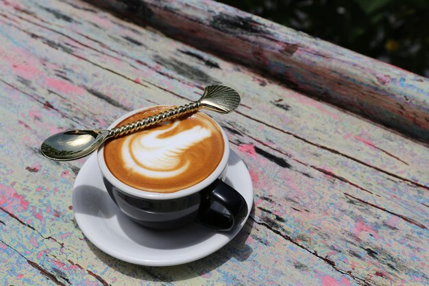 Tasse leckerer Cappuccino mit Latte Art und goldenem Löffel auf Holztischhintergrund