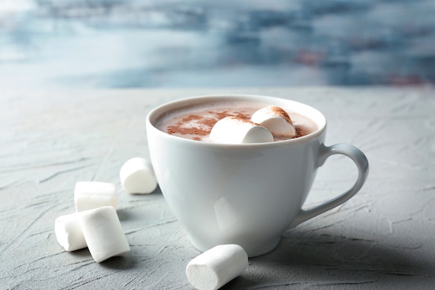 Tasse leckeres Kakaogetränk mit Marshmallow auf strukturiertem Tisch