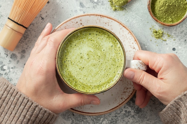 Tasse Matcha-Grüntee in Frauenhänden.