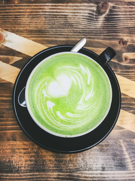 Tasse Matcha Latte in schwarzer Tasse auf Holzhintergrund