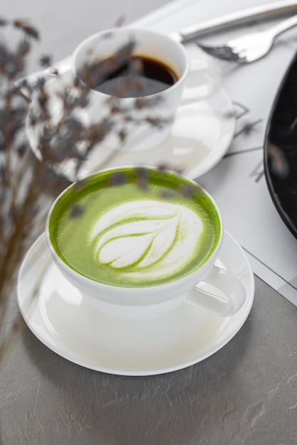 Tasse Matcha Latte und Kaffee. Foto in hoher Qualität. Matcha, grüner Tee Latte in einer Tasse. Grauer Hintergrund. Nahansicht. Ansicht von oben.