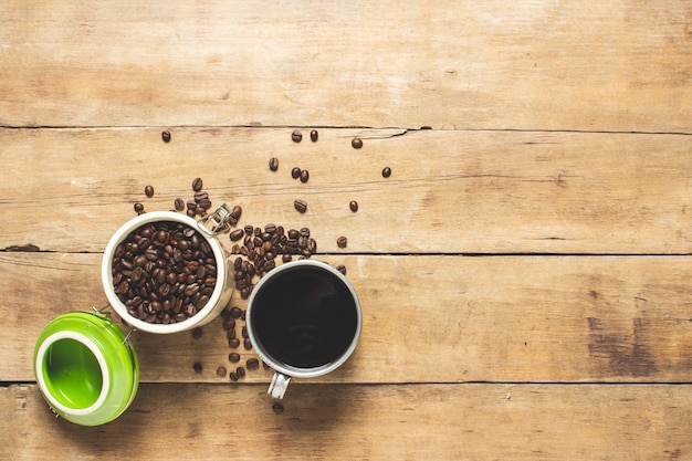 Tasse mit frischem Kaffee und eine Dose mit Kaffeekörnern, Kaffeebohnen liegen auf einem Holztisch.