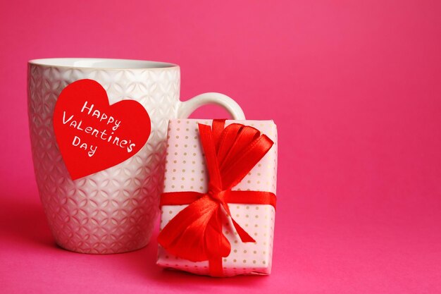 Tasse mit Grußkarte und Geschenkbox zum Valentinstag auf rosa Hintergrund