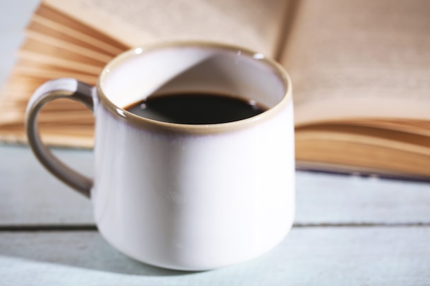 Tasse mit heißem Kaffee und altem Buch auf Holztisch