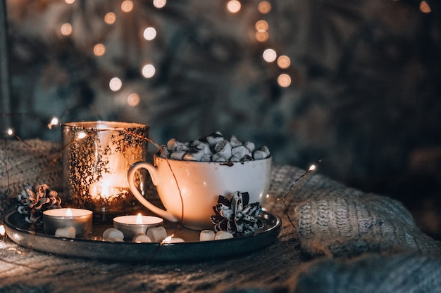 Tasse mit heißem Winterkakao und Marshmallows auf dem Bett Weihnachtsbeleuchtung Tannenzapfen Dekoration