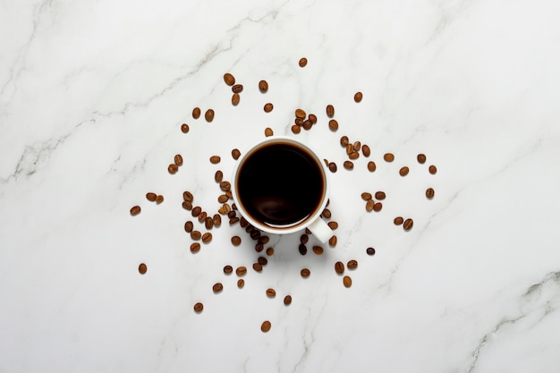 Tasse mit Kaffee und Kaffeekörnern auf einem Marmortisch. Konzept Frühstück, schwarzer Kaffee, Kaffee für die Nacht, Schlaflosigkeit. Flache Lage, Draufsicht