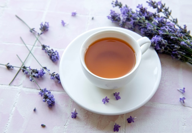 Tasse mit Lavendeltee und frischen Lavendelblüten auf rosafarbenem Fliesenhintergrund