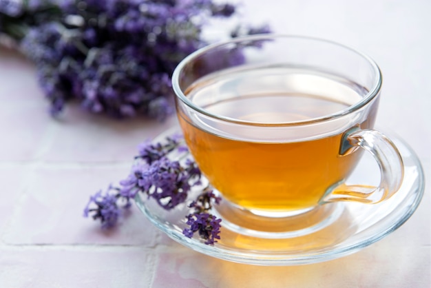 Tasse mit Lavendeltee und frischen Lavendelblüten auf rosafarbenem Fliesenhintergrund