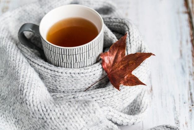 Foto tasse mit tee in gestricktem schal mit ahornblatt