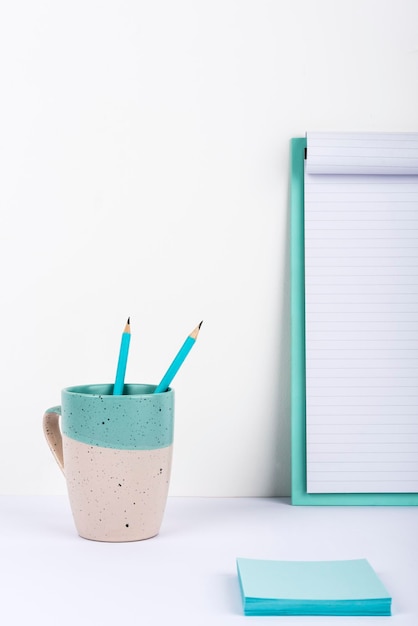 Tasse mit zwei Bleistiften auf dem Schreibtisch mit Zwischenablage mit wichtigen Nachrichten und Notizen