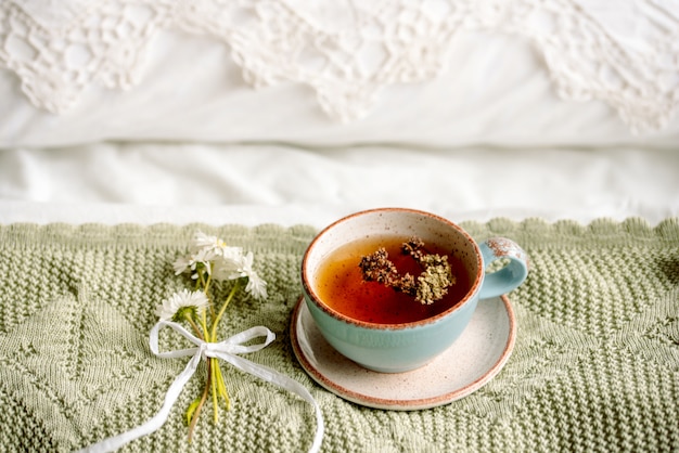 Tasse natürlichen Kräutertee aus Minze und Zitronenmelisse im Bett, morgens hautnah. Gemütliche Atmosphäre.Openwork Spitze, Baumwolle weiße Decke, Sommer Gänseblümchen Blumen.Frühstück.Provence und Retro-Stil.