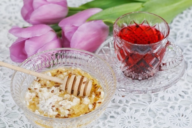 Tasse roter Karkadeh-Tee, Hüttenkäse plus Haferflocken, Leinsamen und Honig auf dem Tisch mit lila Tulpen