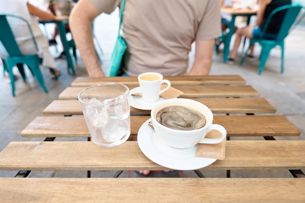 Tasse schwarzen Kaffee und ein Glas mit Eis auf einer Tischbar im Freien