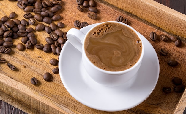 Tasse schwarzen Kaffee und Kaffeebohnen auf hölzernem Hintergrund.