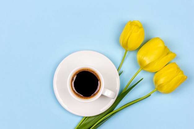 Tasse schwarzen kaffees auf einer untertasse und einem blumenstrauß gelbe tulpenblumen auf einer blauen hintergrundoberansicht