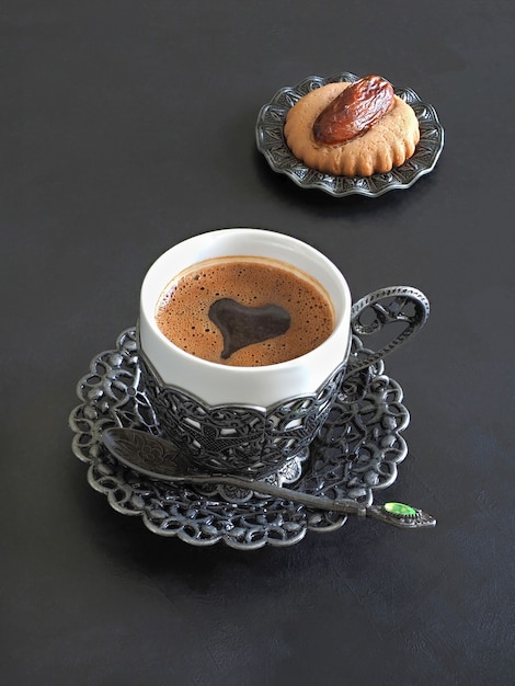 Tasse schwarzen Kaffees mit Herzform und arabischen Süßigkeiten auf schwarzem Tisch