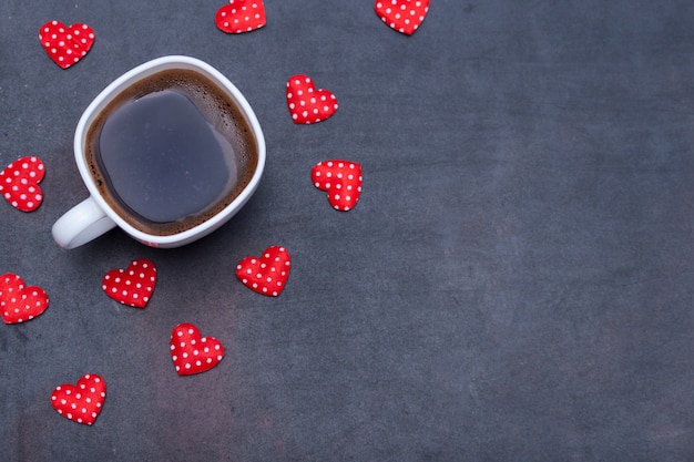 Tasse schwarzen Kaffees und Herzen auf schwarzem Hintergrund.