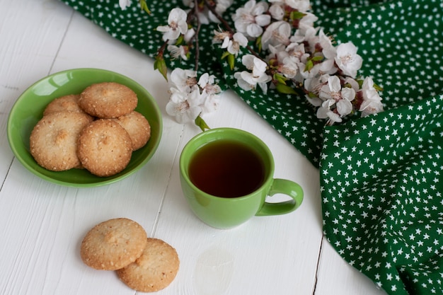 Tasse schwarzen Tee auf einer grünen Serviette, hausgemachte Kekse, ein Zweig der Aprikosenblüte