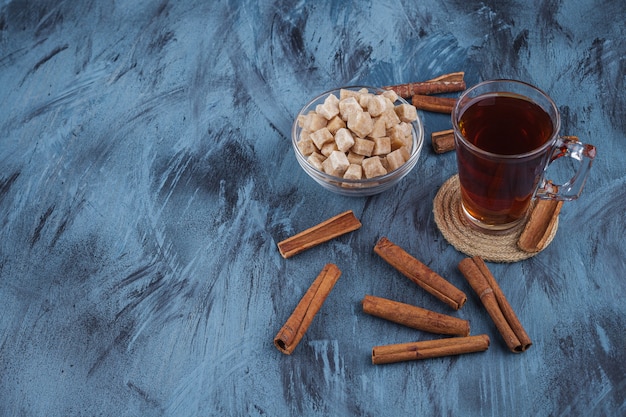 Foto tasse schwarzen tee mit schüssel braunem zucker auf blauem hintergrund.