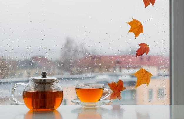 Tasse Tee auf der Fensterbank mit Herbstlaub auf der Fensterscheibe