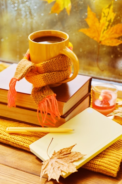 Tasse Tee Herbstlaub Bücher Notizbuch und rot gestricktes Plaid auf Holztisch