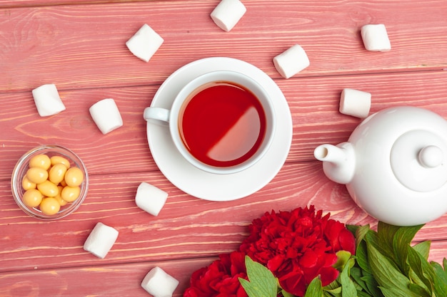 Tasse Tee mit Bonbons und Blumen auf Holztisch