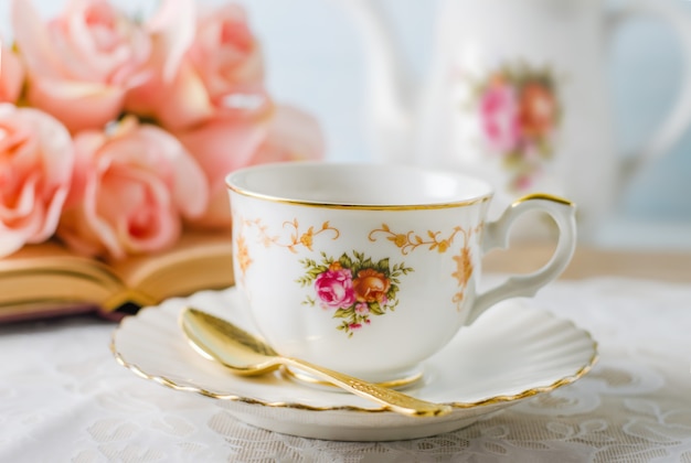 Tasse Tee mit Buch, Teekanne und rosafarbenen Blumen auf Blau