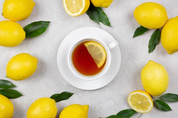 Tasse Tee mit frischen Zitronen und Blättern auf hellgrauem Betonhintergrund. Heißes gesundes Getränk. Immunabwehr, Vitamin C. Ansicht von oben.