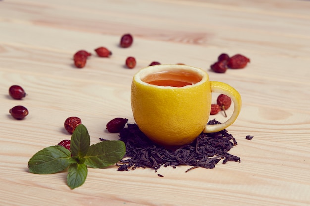 Tasse tee mit hippen rosen, auf holztisch. eine tasse aus echter zitrone