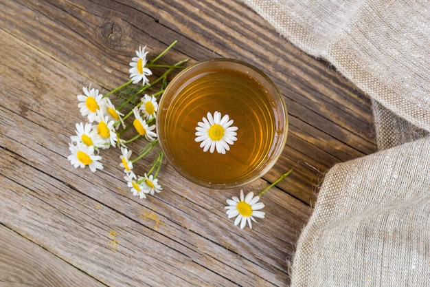 Tasse Tee mit Kamillenblumen auf rustikaler Tabelle