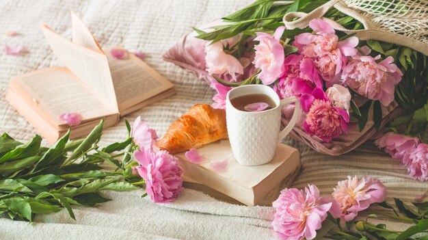 Tasse Tee mit Pionsblumen und Frühlingsdekor auf den Büchern