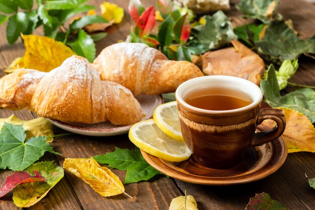 Tasse Tee mit Zitrone, Hörnchen, Herbstfall verlässt