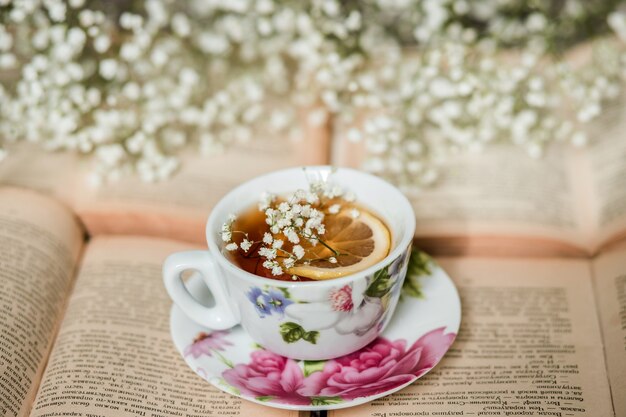 Tasse Tee mit Zitrone und geöffnetes Buch auf dem Tisch im Zimmer