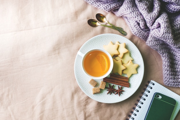 Tasse Tee mit Zitrone und Plätzchen, Honig und Zimtstangen, Sternanis auf der Decke