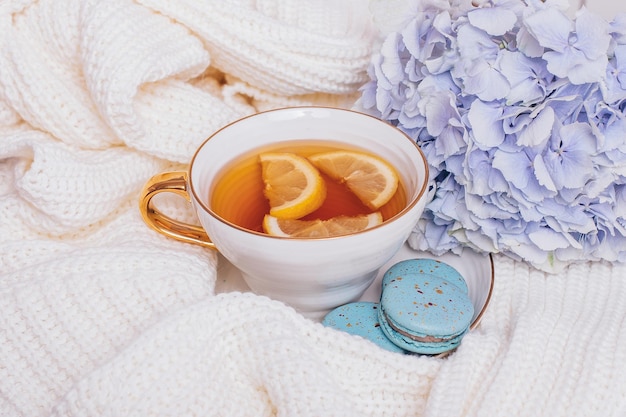 Tasse Tee mit zitronensüßen Makronen und Hortensienblüte auf Wollhintergrund