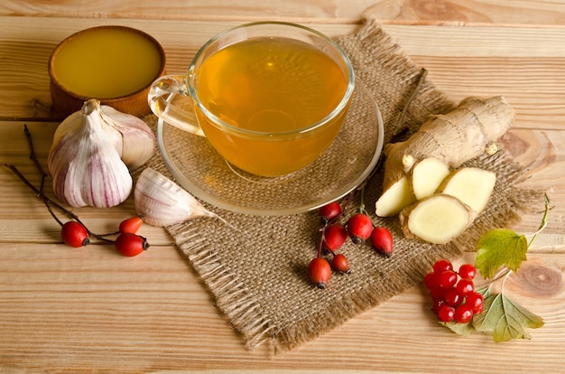 Tasse Tee, Scheiben Ingwer, Honig, Hagebuttenbeeren und Viburnum auf einem Holztisch